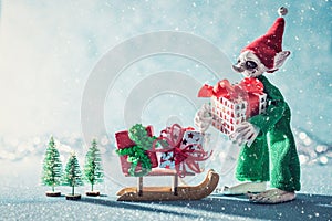 Cute Cheerful Santas Helper Elf Loading Christmas Gifts Onto Santas Sleigh. North Pole Christmas Scene. Santas Workshop.