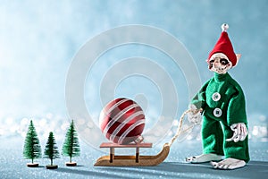 Cute Cheerful Santas Helper Elf Pulling Santas Sleigh With Christmas Bauble.North Pole Christmas Scene. Elf at work.