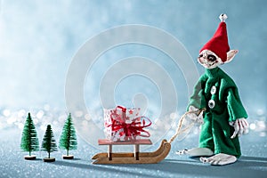 Cute Cheerful Santas Helper Elf Pulling Santas Sleigh With Christmas Present. North Pole Christmas Scene. Santas Workshop.