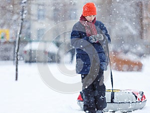 Cute, cheerful young boy in hat, blue jacket plays with snow, has fun, smiles, makes snowman in winter park.