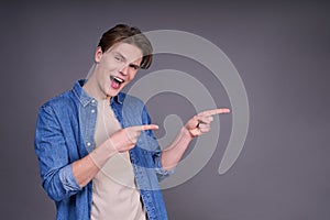 Cute cheerful young man in a denim shirt shows fingers to the side