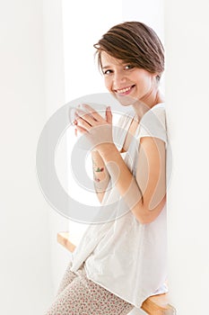 Cute cheerful young woman in pajamas drinking tea