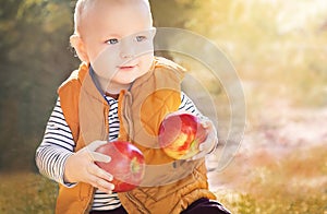 Cute child (baby boy) with two red apples in the sunny autumn (fall) day. Kid eating healthy food, snack.