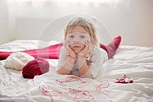 Cute child, blond boy, playing with white and red bracelet