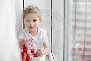 Cute child, blond boy, playing with white and red bracelet, martenitsa