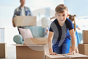 Cute child with box with his family packing belongings at home. Moving into new house