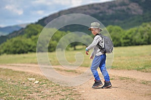 Cute child boy with backpack walking on a little path in mountains. Hiking kid