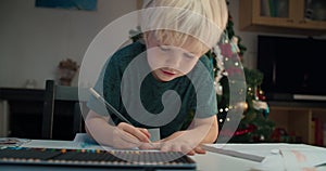 Cute child boy drawing with pencil sitting at the table on Christmas holidays