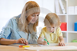Cute child boy drawing and writing with colorful markers pens at kindergarten. Creative kid painting at playschool. Teacher helps photo