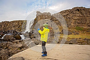 Cute child, boy, enjoying a sunny day in Thingvellir National Park rift valley,taking pictures with cellphone, Iceland