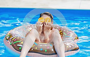 Cute child boy on funny inflatable donut float ring in swimming pool with oranges. Teenager learning to swim