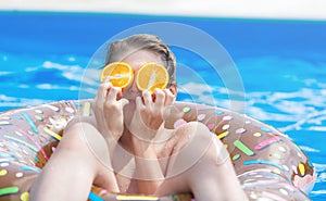 Cute child boy on funny inflatable donut float ring in swimming pool with oranges. Teenager learning to swim