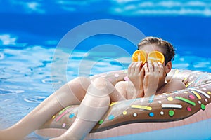 Cute child boy on funny inflatable donut float ring in swimming pool with oranges. Teenager learning to swim