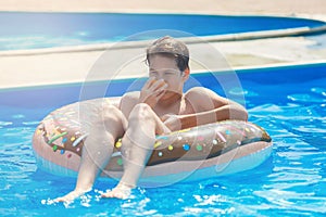 Cute child boy on funny inflatable donut float ring in swimming pool with oranges. Teenager learning to swim,