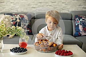 Cute child, boy with pet dog, eating fried doughnuts at home with his siblings