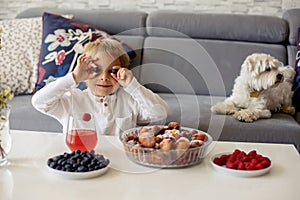 Cute child, boy with pet dog, eating fried doughnuts at home with his siblings