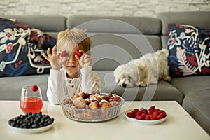 Cute child, boy with pet dog, eating fried doughnuts at home with his siblings