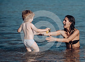 Cute child boy play with mom in sea, ocean. Mom and kid with smiling faces spend time together in sea on sunny day