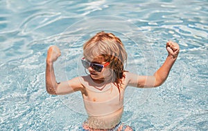 Cute child boy show muscles, swim in swimming pool, summer water background with copy space. Funny kids face.