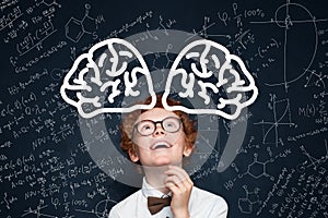 Cute child boy student in glasses having fun against blackboard background with science formulas
