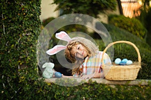 Cute child bunny wear rabbit ears in garden, Happy Easter day. Bunny boy with easters basket, funny outdoor portrait