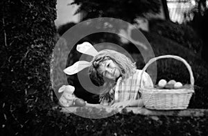 Cute child bunny wear rabbit ears in garden, Happy Easter day. Bunny boy with easters basket, funny outdoor portrait