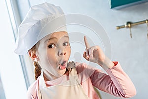 cute child in chef hat pointing up with finger and looking at camera