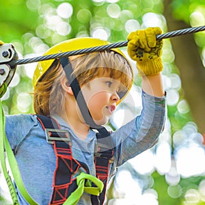 Cute child in climbing safety equipment in a tree house or in a rope park climbs the rope. Happy little child climbing