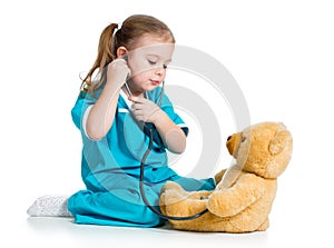 Cute child with clothes of doctor examining teddy bear toy