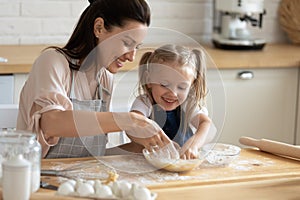 Cute child daughter helping mum kneading dough together in kitchen