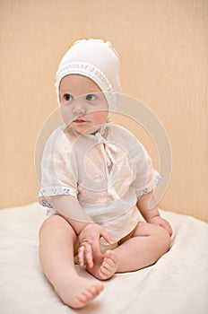 Cute child dressed in white sits on the bed touchi