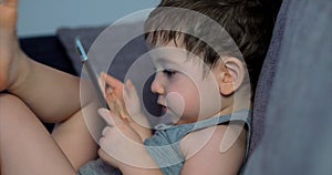 Cute Child Entertaining With Tablet. Little Boy Spending Leisure Time Playing Mobile Game in the and Crushes the Bright