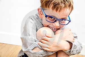 Cute child giggling, hiding his missing tooth mouth in knees
