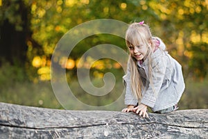 Cute child girl on all fours balances on a fallen log