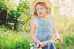 Cute child girl with bicycle on summer sunny road