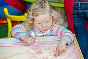 Cute child girl drawing draws developing sand in preschool