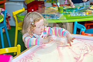 Cute child girl drawing draws developing sand in preschool at table in kindergarten