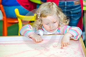 Cute child girl drawing draws developing sand in preschool at table in kindergarten
