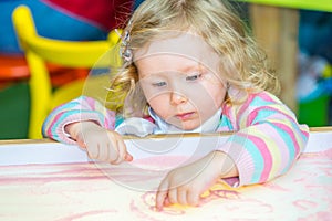 Cute child girl drawing draws developing sand in preschool at table in kindergarten