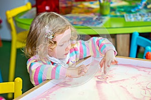 Cute child girl drawing draws developing sand in preschool at table in kindergarten