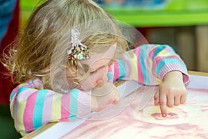 Cute child girl drawing draws developing sand in preschool at table in kindergarten