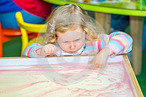 Cute child girl drawing draws developing sand in preschool at table in kindergarten