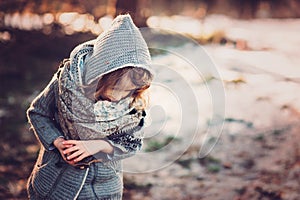 Cute child girl in grey knitted coat plays on the walk in winter forest