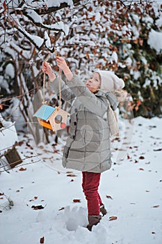 Cute child girl hangs bird feeder in winter snowy garden