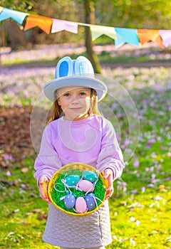 cute child girl in hat with rabbit ears o and a basket with Easter eggs at the party in park