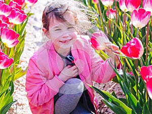 Cute child girl with long hair smelling tulip flower on tulip fields in Amsterdam region, Holland, Netherlands