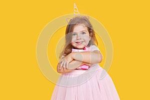 Cute child girl model with wavy hair in elegant pink dress posing on a yellow  background.