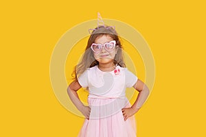 Cute child girl model with wavy hair in elegant pink dress posing on a yellow isolated background.