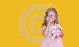 Cute child girl model with wavy hair in elegant pink dress posing on a yellow isolated background.