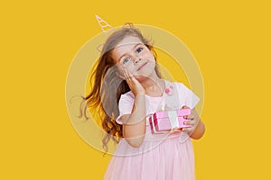 Cute child girl model with wavy hair in elegant pink dress posing on a yellow isolated background. Concept for advertising